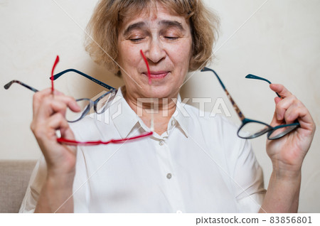An elderly Caucasian woman chooses glasses from her home collection 83856801