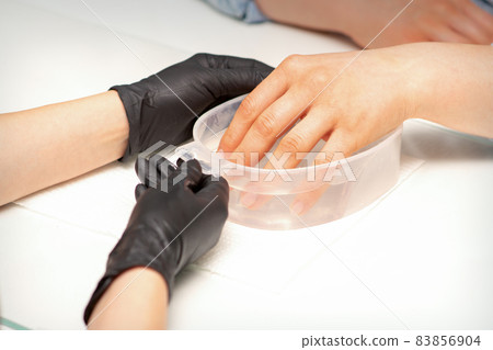 The female dipped her hand in a bowl of water softening nails preparing for the manicure. The female dipped her hand in a bowl of water softening nails preparing for the manicure. 83856904