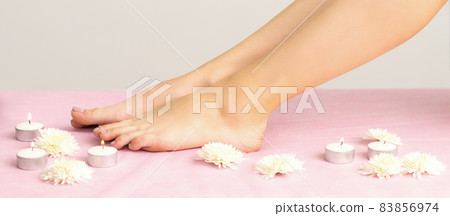 Beautiful white smooth feet of young woman with candles and flowers on pink couch. Beautiful white smooth feet of young woman with candles and flowers on pink couch. 83856974