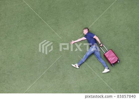 Young man with suitcase walking on green grass top view Young man with suitcase walking on green grass top view 83857840