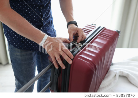 Man closing suitcase with combination lock at home closeup 83857870