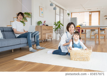 A mom who folds laundry in the living room at home, an elementary school girl who helps, and a dad who works on a computer on the sofa A mom who folds laundry in the living room at home, an elementary school girl who helps, and a dad who works on a computer on the sofa 83857871