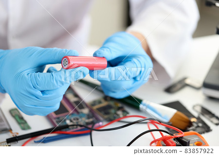 Master holding electronic battery near microchips in workshop closeup Master holding electronic battery near microchips in workshop closeup 83857922