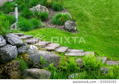stone staircase with steps made of wild natural stone on slope of hill park landscape with rock, ground garden lantern among green plants in summer environment for eco travel, nobody. 83859283