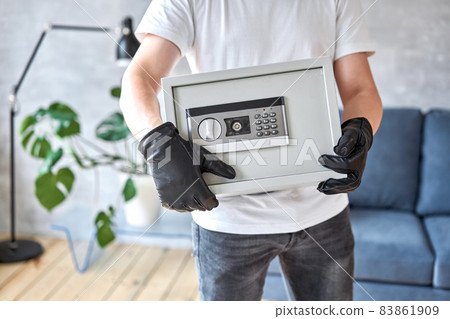 Thief with black mask stealing modern Metal safe with an electronic lock. Home theft of money and documents concept. 83861909