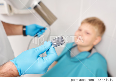 Doctor pointing X-ray unit holding electronic sensor in child. Dentist prepares boy for tooth x-ray image in dental clinic. Doctor pointing X-ray unit holding electronic sensor in child. Dentist prepares boy for tooth x-ray image in dental clinic. 83861919
