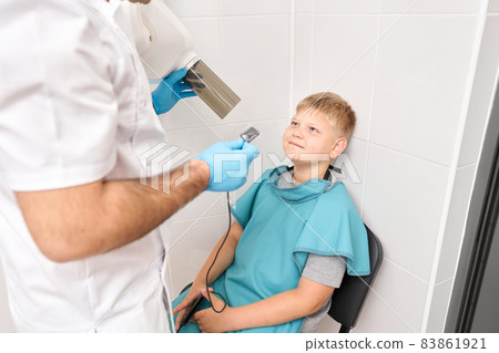 Radiographer taking teeth radiography to a boy using digital x-ray machine in pediatric dental clinic. Dentist prepares boy for tooth x-ray image in dental clinic. Radiographer taking teeth radiography to a boy using digital x-ray machine in pediatric dental clinic. Dentist prepares boy for tooth x-ray image in dental clinic. 83861921
