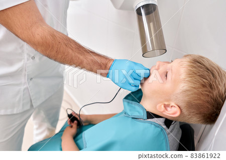 Radiographer taking teeth radiography to a boy using digital x-ray machine in pediatric dental clinic. Dentist prepares boy for tooth x-ray image in dental clinic. 83861922