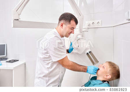 Radiographer taking teeth radiography to a boy using digital x-ray machine in pediatric dental clinic. Dentist prepares boy for tooth x-ray image in dental clinic. Radiographer taking teeth radiography to a boy using digital x-ray machine in pediatric dental clinic. Dentist prepares boy for tooth x-ray image in dental clinic. 83861923