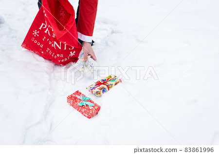 A man dressed as Santa Claus collects gifts in a snowy forest in the snow, colorful boxes with gifts. 83861996