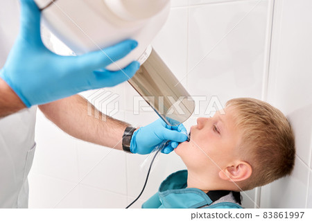 Radiographer taking teeth radiography to a boy using digital x-ray machine in pediatric dental clinic. Dentist prepares boy for tooth x-ray image in dental clinic. 83861997