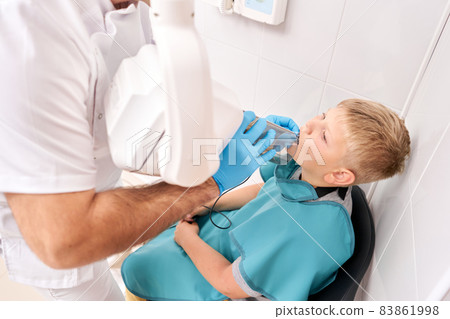 Radiographer taking teeth radiography to a boy using digital x-ray machine in pediatric dental clinic. Dentist prepares boy for tooth x-ray image in dental clinic. 83861998