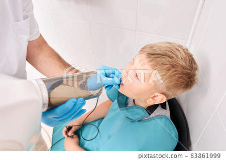 Radiographer taking teeth radiography to a boy using digital x-ray machine in pediatric dental clinic. Dentist prepares boy for tooth x-ray image in dental clinic. Radiographer taking teeth radiography to a boy using digital x-ray machine in pediatric dental clinic. Dentist prepares boy for tooth x-ray image in dental clinic. 83861999