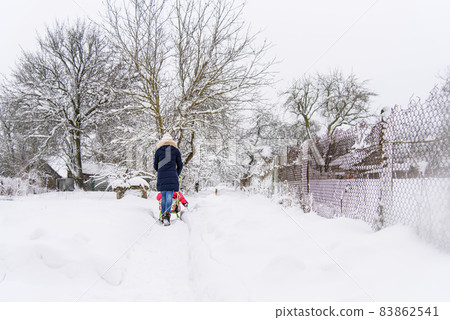 Mom walks with her child in the snow on a sled. Woman sledding a child. Winter time 83862541