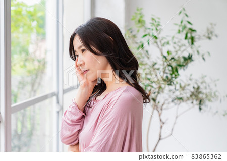 A sick woman standing by the window wearing a loungewear A sick woman standing by the window wearing a loungewear 83865362