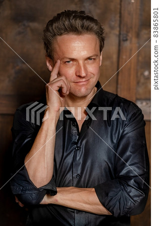 Successful Rock Star has a Photo Shoot for a Famous Magazine. Magazine Cover. Stylish Blonde Man in Sexy Black Shirt Posing and Looking at Camera Isolated on Wood Background. Wood Background. 83865801