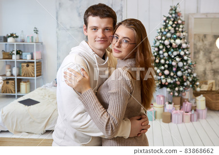 A couple hugs in front of bedroom with Christmas tree on New Year Eve. 83868662
