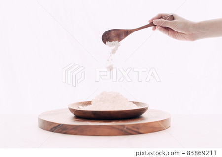 Hand pouring flour into wooden bowl with wooden spoon Hand pouring flour into wooden bowl with wooden spoon 83869211