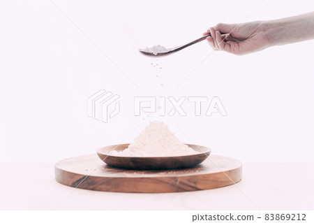 Hand pouring flour into wooden bowl with wooden spoon Hand pouring flour into wooden bowl with wooden spoon 83869212