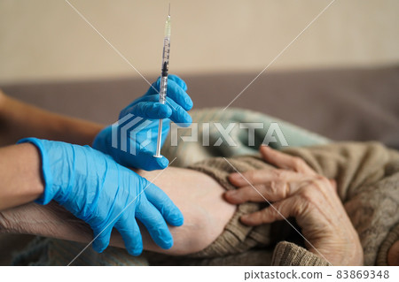 The nurse makes an injection with the vaccine to the patient at home. 83869348