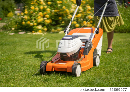 A young girl is mowing a lawn in the backyard with an orange lawn mower. A young girl is mowing a lawn in the backyard with an orange lawn mower. 83869977