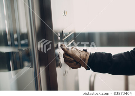 Close up of hand in glove forefinger pressing the button elevator during coronavirus pandemic covid-19 quarantine concept 83873404