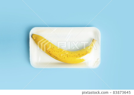 Fruits in plastic packaging from the supermarket are minimal. Banana in cellophane and non-degradable plastic on a blue background. Biodegradable product packaging, environmental protection, nature Fruits in plastic packaging from the supermarket are minimal. Banana in cellophane and non-degradable plastic on a blue background. Biodegradable product packaging, environmental protection, nature 83873645