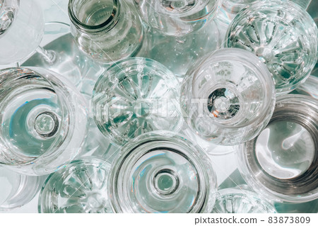 Beautiful different glasses stand on white background in sunlight and create shadows. Hard light, long shadows. Creative concept of drinks, alcohol cocktails. Glassware concept 83873809