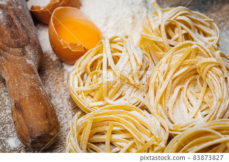 Fresh pasta food. Homemade Italian pasta cooked on a wooden background in a rustic style decorated with egg and flour. 83873827