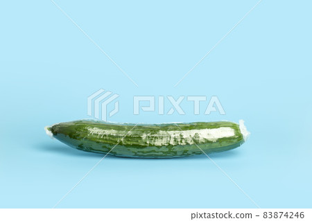 Vegetables in plastic packaging from the supermarket are minimal. Cucumber in cellophane and non-degradable plastic on a blue background. Biodegradable product packaging, environmental protection 83874246
