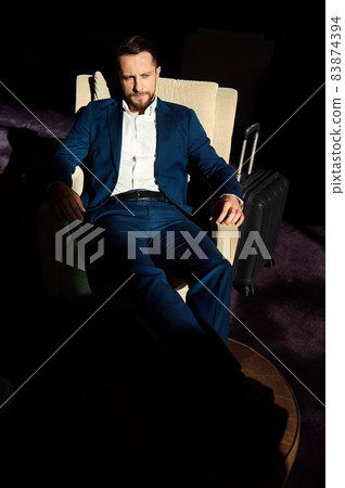 High angle view of a successful young businessman at business trip, relaxing on an armchair with outstretched crossed legs on an ottoman in lounge bar of a luxury hotel 83874394