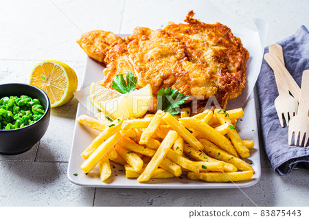 Fish and chips with green peas on gray tile background. British cuisine concept. Fish and chips with green peas on gray tile background. British cuisine concept. 83875443