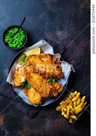 Fish and chips with green peas on dark background. British cuisine concept. Fish and chips with green peas on dark background. British cuisine concept. 83875444