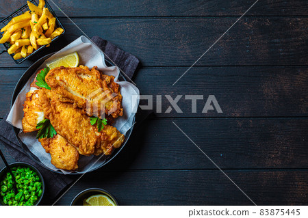 Fish and chips with green peas on dark background. British cuisine concept. Fish and chips with green peas on dark background. British cuisine concept. 83875445