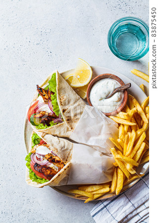Chicken gyros with vegetables, french fries and tzatziki sauce on plate. Greek food concept. Chicken gyros with vegetables, french fries and tzatziki sauce on plate. Greek food concept. 83875450
