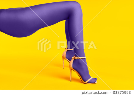 Long slim legs of young woman in purple tights and stylish high heels shoes on yellow background. Long slim legs of young woman in purple tights and stylish high heels shoes on yellow background. 83875998