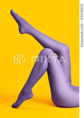 Long legs of beautiful young woman in bright tights relax on yellow background 83876078