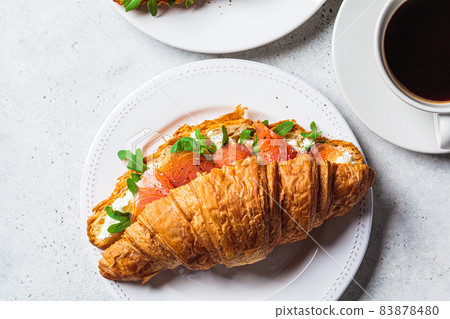 Croissant sandwich with cream cheese, salmon and arugula on white plate, gray background. Healthy breakfast concept. 83878480