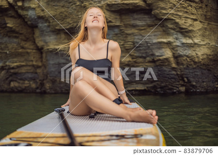 Young women Having Fun Stand Up Paddling in the sea. SUP. Red hair girl Training on Paddle Board near the rocks Young women Having Fun Stand Up Paddling in the sea. SUP. Red hair girl Training on Paddle Board near the rocks 83879706