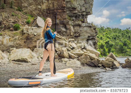 Young women Having Fun Stand Up Paddling in the sea. SUP. Red hair girl Training on Paddle Board near the rocks 83879723
