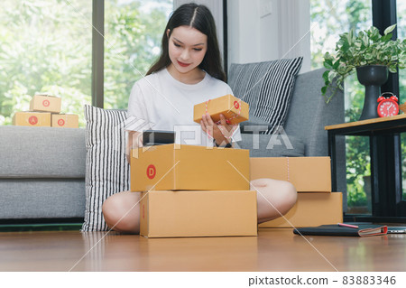 A woman using a calculator to calculate the price of items. Successful entrepreneur business woman with online sales and Parcel shipping in her home office. A woman using a calculator to calculate the price of items. Successful entrepreneur business woman with online sales and Parcel shipping in her home office. 83883346