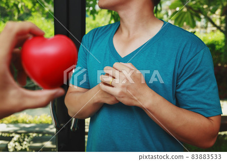 Man clutching his chest from acute pain. Red heart ball foam on hand. Heart attack symptom-Healthcare and medical concept. 83883533