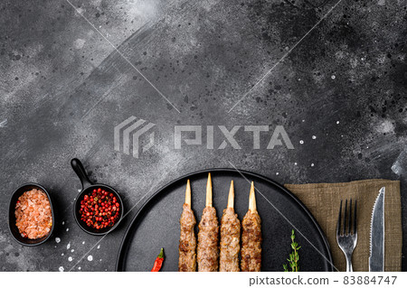 Shish kebab on a stick, from ground land mutton meat, on plate, on black dark stone table background, top view flat lay, with copy space for text 83884747