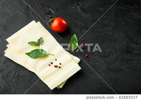 Lasagna dough sheets, with seasoning and herb, on black stone background, with copy space for text 83885037