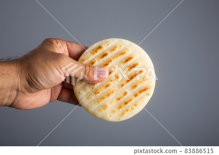Man holds traditional Venezuelan food arepa made from cornmeal Man holds traditional Venezuelan food arepa made from cornmeal 83886515