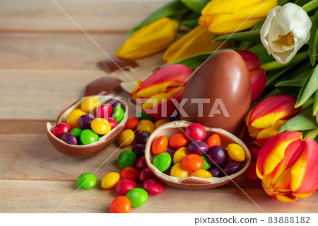 Beautiful red and yellow tulips for easter holiday. Chocolate eggs and candies on a wooden background. Festive design for postcards, copy space Beautiful red and yellow tulips for easter holiday. Chocolate eggs and candies on a wooden background. Festive design for postcards, copy space 83888182