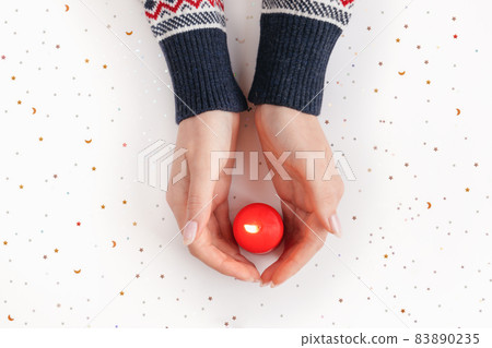 Female hands in sweater with red burning candle. Winter holiday, Christmas or Valentine's day background. Giving warmth and love concept. Xmas backdrop for design projects, postcards. New Year theme 83890235