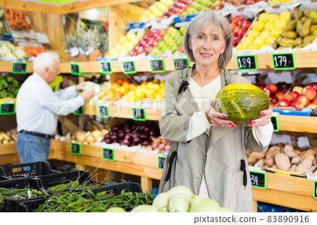 Woman choosing melon in greengrocer Woman choosing melon in greengrocer 83890916