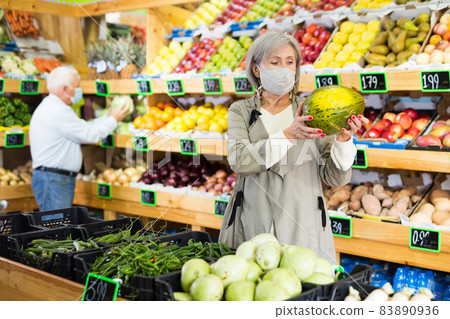 Woman in mask choosing melon in greengrocer 83890936