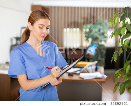 Young woman therapist writes notes on a tablet, standing in a office 83892561
